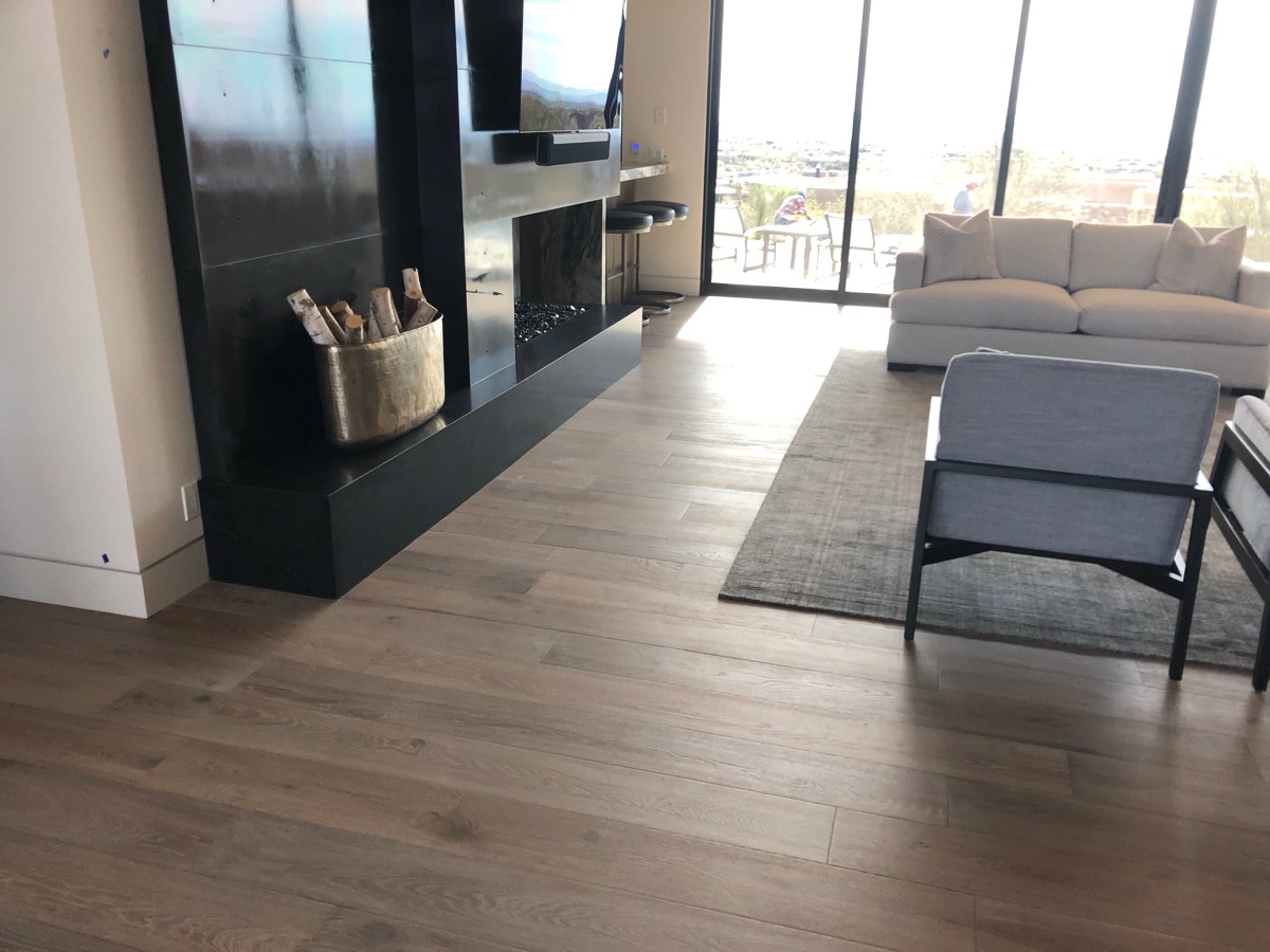 Wide plank floor beneath a black stone fireplace and mountain view