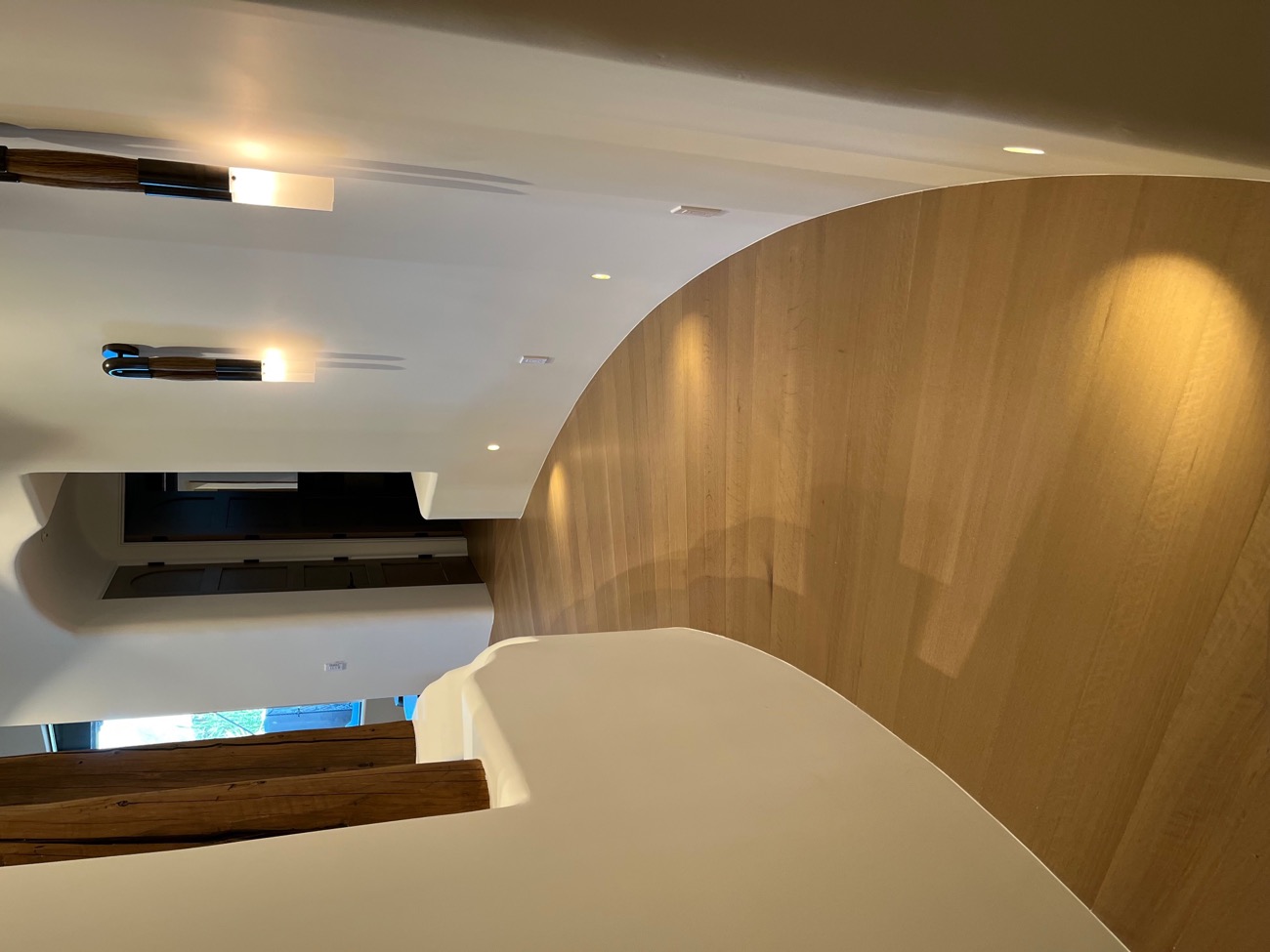Curved white hallway with light white-oak flooring lit by warm sconces